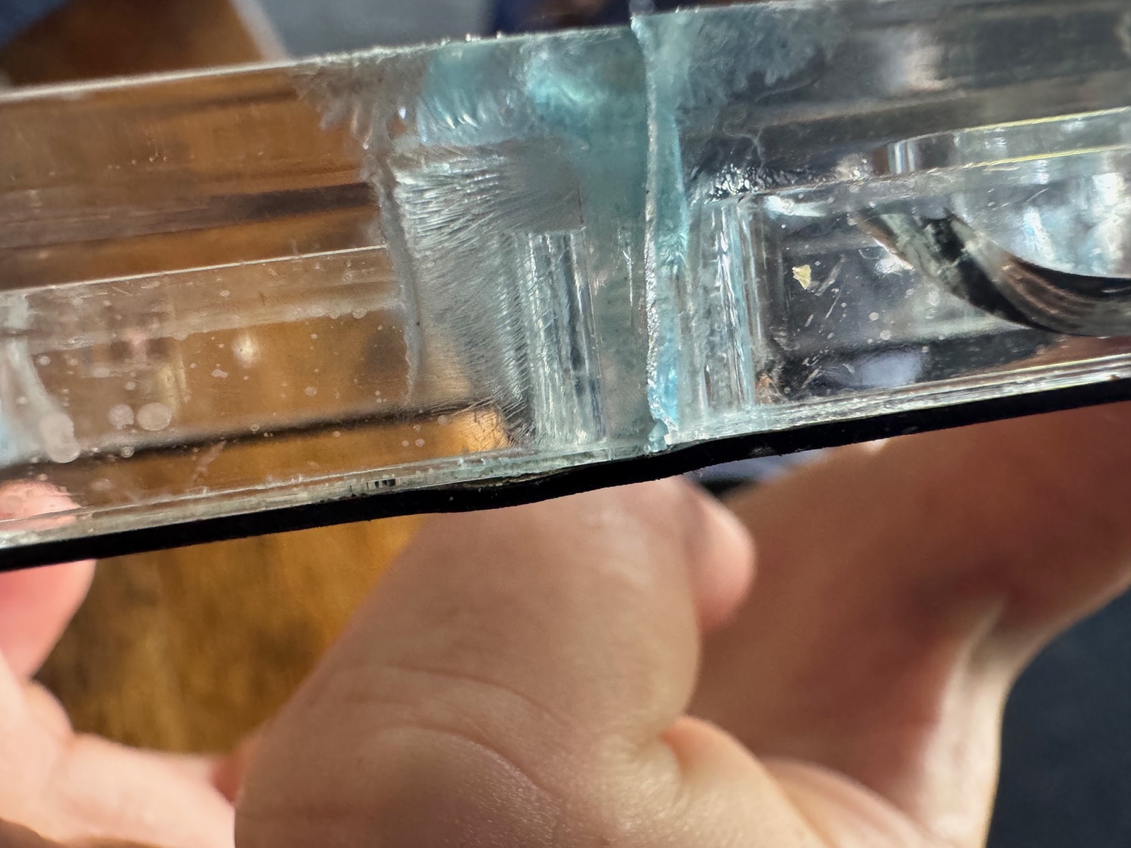 Close-up of the edge of a clear cover, with a fan of fine cracks radiating from a screw hole